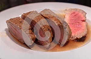 medium rare roasted pork fillet with a wine and balsamico sauce, cut into tasty slices and put on a white plate.