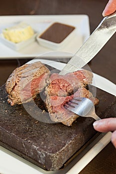 Medium rare steak sizzling on hot stone plate being sliced