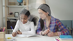 Medium shot of asian happy woman tutor teaching and helping her black african american girl student at home.