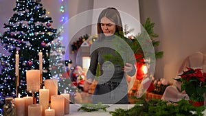 Medium shot of beautiful woman choosing fir tree for handmade New Year wreath cutting branch with pruning scissors