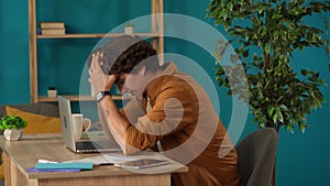 Medium shot capturing a man working on a laptop in his home office and drinking coffee. Young male programmer is rubbing