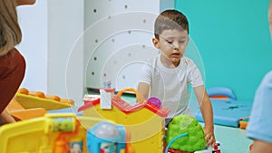 medium shot of the cutest little boy playing with plastic toys with his teacher at the nursery