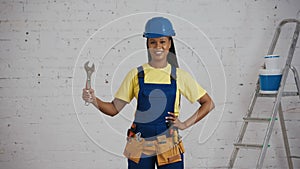 Medium shot of a dark-skinned young female construction worker standing in the room, wearing a tool belt, showing an