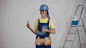 Medium shot of a dark-skinned young female construction worker standing in the room, wearing a tool belt, showing a