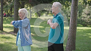 Medium shot fit senior couple warming up exercising simultaneously in sunny park outdoors. Confident happy Caucasian