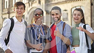 Medium shot four happy students looking at camera smiling showing thumbs up simultaneously. Portrait of confident smart