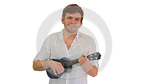 Smiling young man playing ukulele looking into the camera on whi