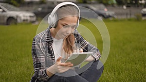 Medium shot. Girl watching funny videos on a tablet. Music in large headphones and scrolls the news on the tablet