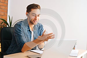 Medium shot of handsome young business man in earphone having online video conference on laptop at home office.