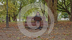 Medium shot of handsome young man working on laptop computer sitting outdoors in park. Male looking away thoughtfully