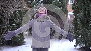 Medium shot of happy teen girl smiling stretching hands spinning as white snow falling in slow motion. Portrait of
