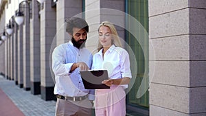 Medium shot portrait of attractive young blonde business woman explaining something on clipboard to male business