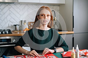 Medium shot portrait of attractive young woman gluing envelopes on board with gifts for children making Christmas advent