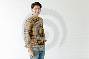 Medium shot portrait of a casual Asian handsome man with cute smiling in a light brown plaid shirt and blue jeans with one hand in
