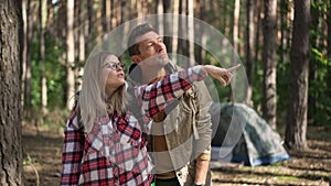 Medium shot portrait of charming woman pointing away talking to man standing in forest in sunshine. Happy confident