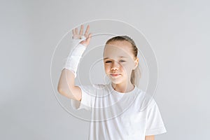 Medium shot portrait of cheerful little girl with broken hand wrapped in white plaster bandage greeting lifting arm