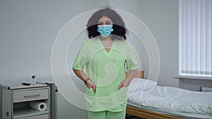 Medium shot portrait of confident doctor in uniform and coronavirus face mask posing in hospital ward. Serious Caucasian