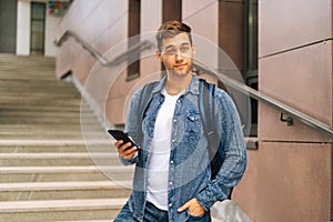 Medium shot portrait of handsome delivery man with thermo backpack holding using mobile phone standing on stairs of