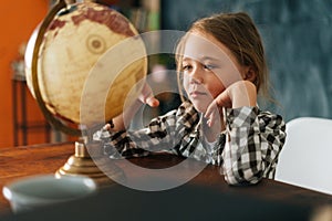 Medium shot portrait of happy curious child girl spinning small globe with interest, looking at countries of world.