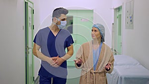 Medium shot portrait of male plastic surgeon in face mask and female patient walking in slow motion along clinic