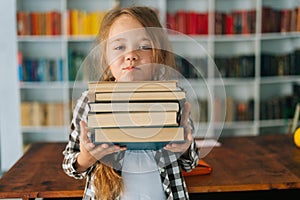 Medium shot portrait of pretty elementary child school girl holding stack of books in library at school looking at