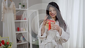Medium shot portrait of slim excited young bride looking in gift box smiling looking at camera. Happy beautiful Middle