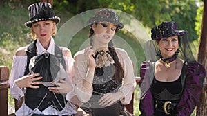 Medium shot portrait of three gorgeous confident Caucasian women in steampunk outfit posing outdoors in sunshine