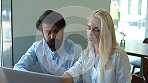 Medium shot portrait of two serious male and female business colleagues sitting at table and talking in cafe looking at