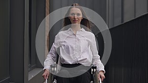 Medium shot portrait of young gorgeous disabled Caucasian woman sitting in wheelchair looking at camera. Successful