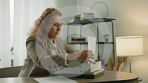 Medium shot of pretty mature woman in glasses inserting paper into typewriter