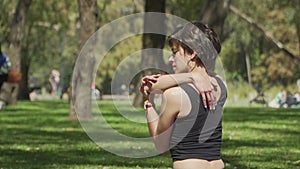 Medium shot of a pretty woman stretching her shoulders at a busy park