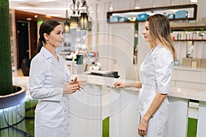 Medium shot of professional female doctor and young nurse talking, standing in clinic lobby. Physicians colleagues