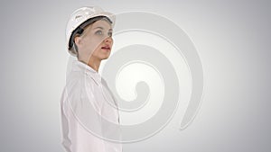 Young woman in hard hat walking and looking around on gradient b