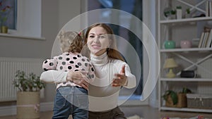 Medium shot of smiling gorgeous millennial mother hugging baby daughter talking. Portrait of joyful Caucasian beautiful