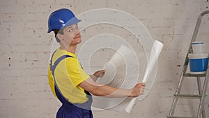 Medium shot of a smiling young construction worker holding a plan of the building. Man seems satisfied, smiling.