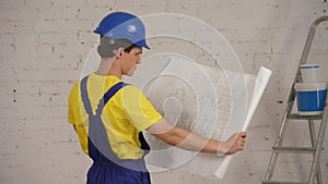 Medium shot of a smiling young construction worker looking at the plan of the building. Man seems concentrated and