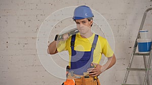 Medium shot of a smiling young construction worker wearing a tool belt, holding a construction water level on his
