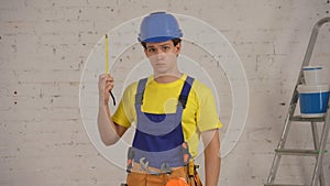 Medium shot of a smiling young construction worker wearing a tool belt, holding an unfolded construction tape measure