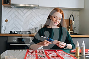 Medium shot of smiling young woman gluing envelopes on board with gifts for children making Christmas advent calendar at