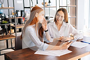 Medium shot of two happy young business women working using digital tablet at meeting desk with job documents at office.