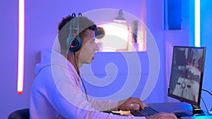 Medium shot of young black gammer in headphones playing in online shooter