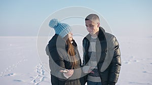 Medium shot of young Caucasian couple searching mobile network signal standing on snowy meadow outdoors. Man and woman