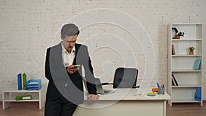 Medium shot of a young man in an office, holding a smartphone in hand, receiving a message, notification with bad news