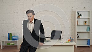 Medium shot of a young man in an office, leaning on the table after receiving a message, notification with bad news. He