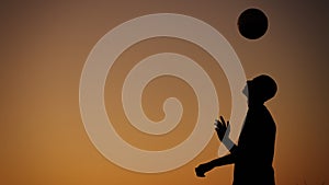 Medium sized photo capturing a silhouette of a teenager, young man playing with a ball outside at sunset. He is throwing