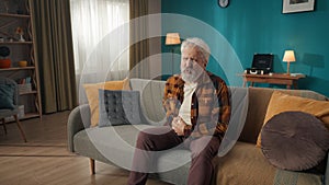 Medium-sized shot of an eldery, retired man, senior citizen sitting on a couch, sofa, feeling severe abdominal pain