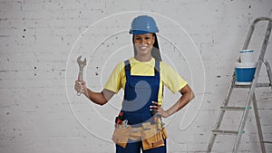 Medium video of a dark-skinned young female construction worker standing in the room, wearing a tool belt, showing an