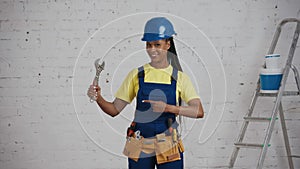 Medium video of a dark-skinned young female construction worker standing in the room, wearing a tool belt, showing an