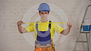 Medium video of a smiling young construction worker wearing a tool belt, unfolding the construction tape measure in