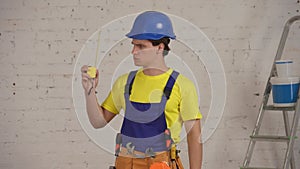 Medium video of a smiling young construction worker wearing a tool belt, unfolding the construction tape measure and